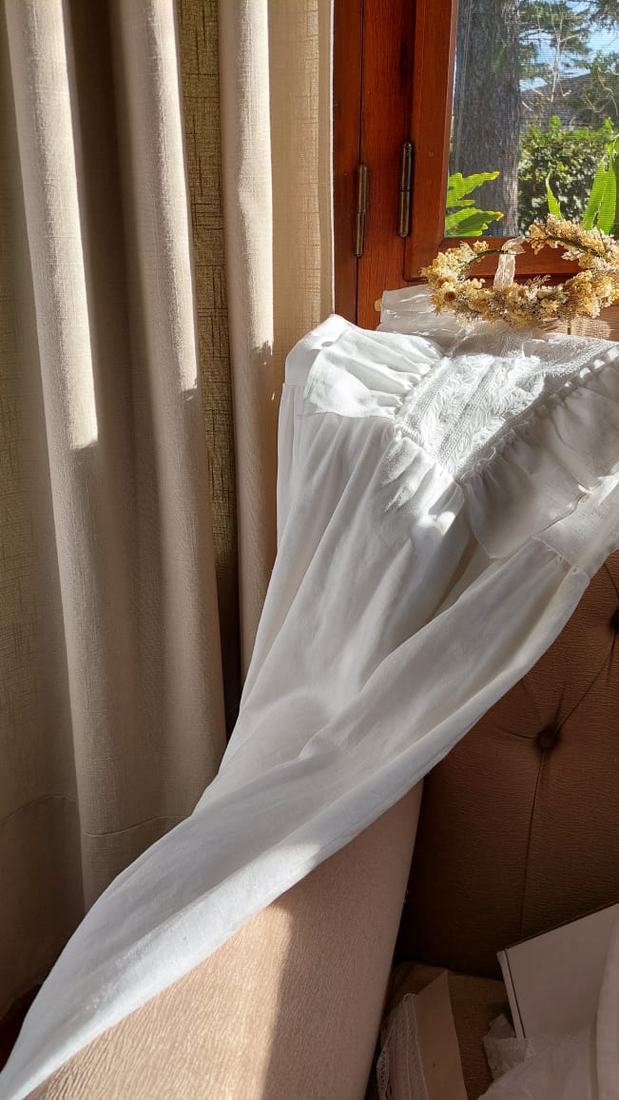Vestido bordado sobre un sillón junto a una corona de flores secas
